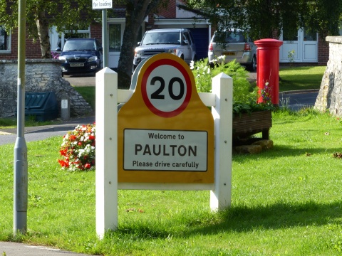 Close up of village gateway sign, with gate feature and yellow backing board.